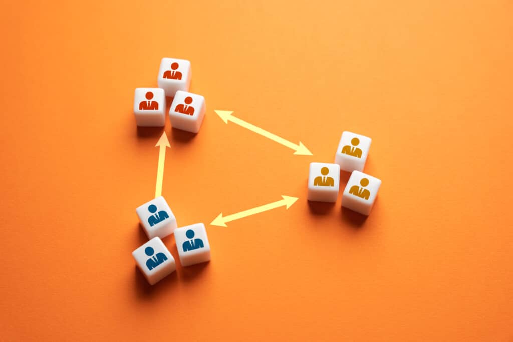 White cubes with red, blue, and yellow human icons are arranged in three groups on an orange background. Yellow arrows connect the groups, illustrating relationships or workflow—perfect for visualizing steps in building an Irish brand.