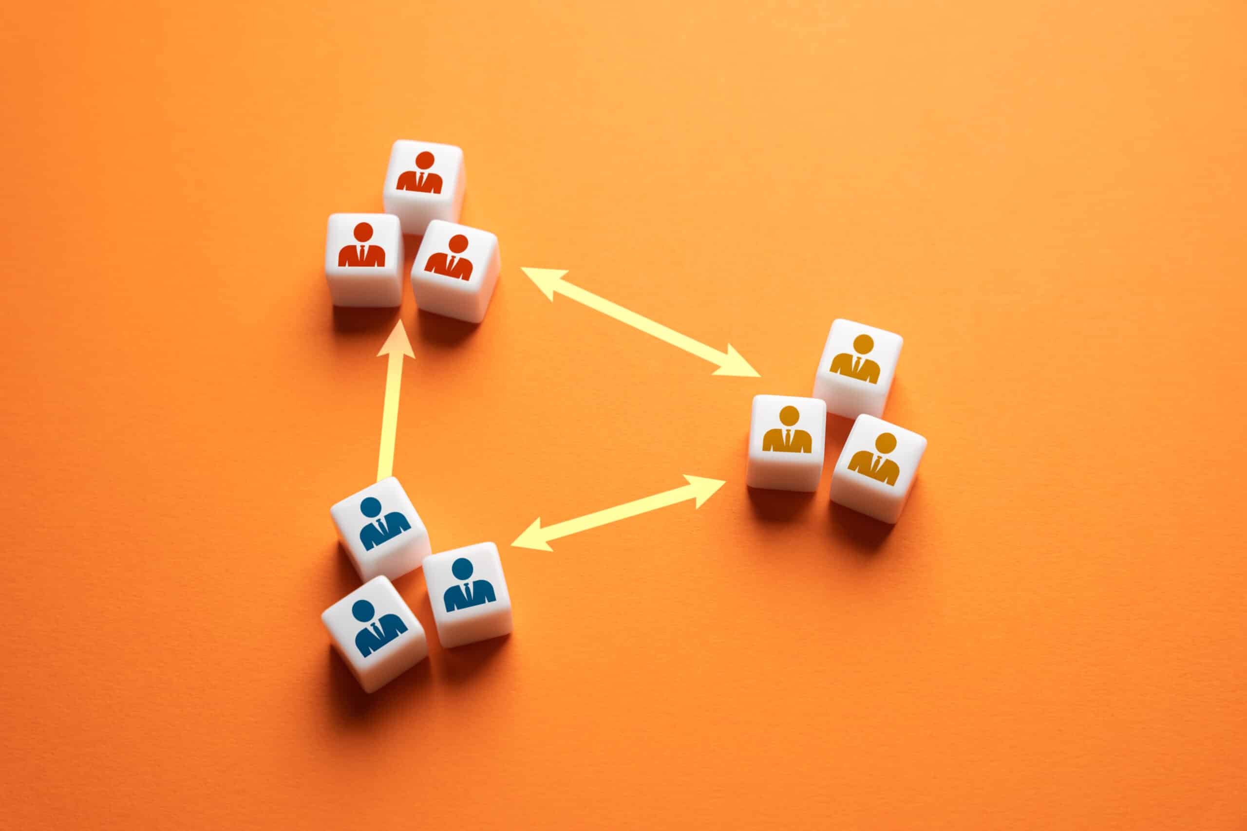 White cubes with red, blue, and yellow human icons are arranged in three groups on an orange background. Yellow arrows connect the groups, illustrating relationships or workflow—perfect for visualizing steps in building an Irish brand.