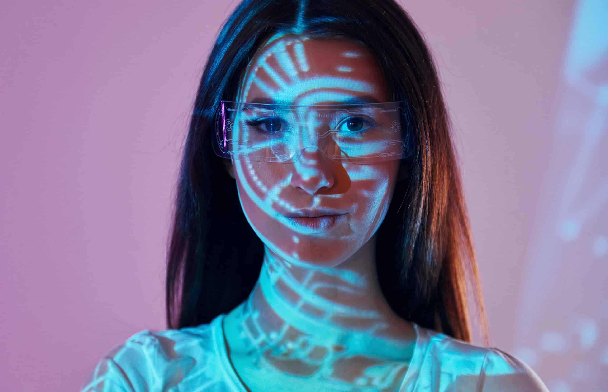 A woman with long brown hair and clear glasses stands in front of a purple background, blue digital patterns and circular graphics projected across her face—evoking the innovation behind building an Irish brand.