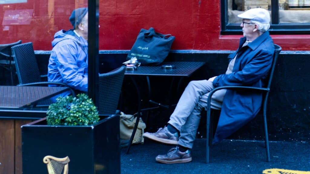Two people sit at tables outside a red building.