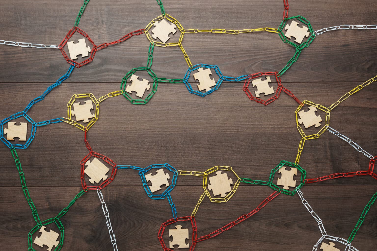 Colorful plastic chains form interconnected networks around wooden puzzle pieces on a dark wooden surface, symbolizing collaboration, teamwork, and the interconnected systems vital for building an Irish brand.