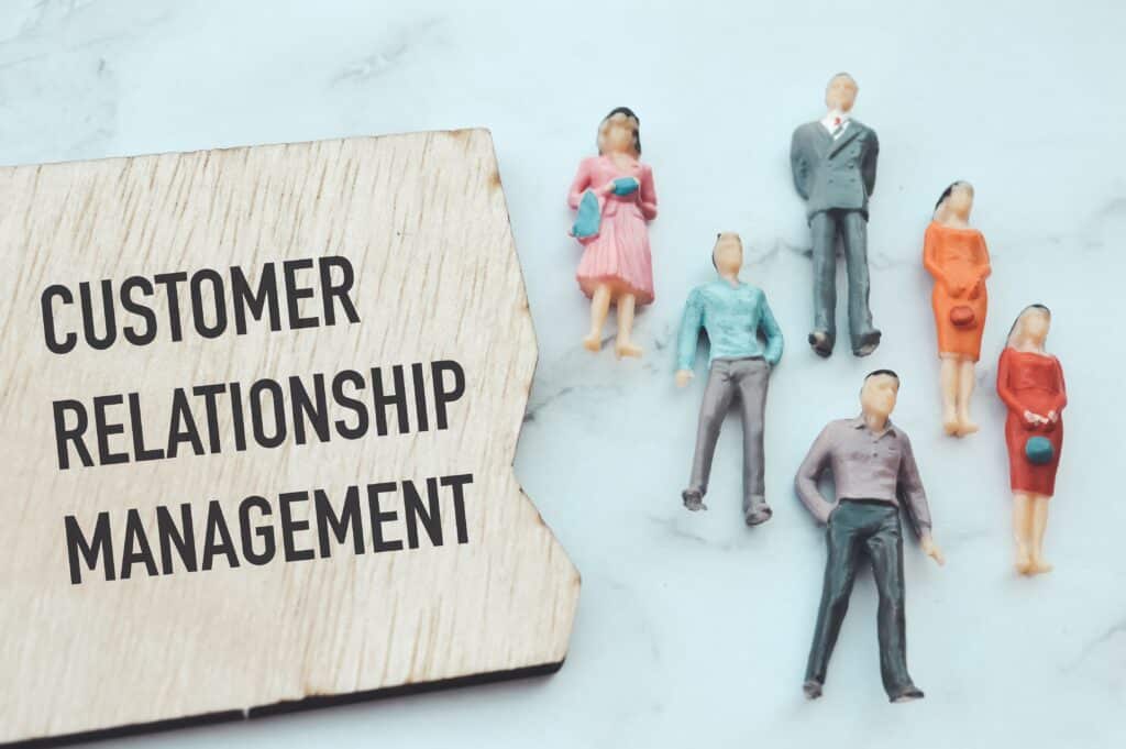 A wooden sign reading Customer Relationship Management beside five miniature figurines of people standing on a light surface, symbolizing CRM, people management concepts, and building an Irish brand.