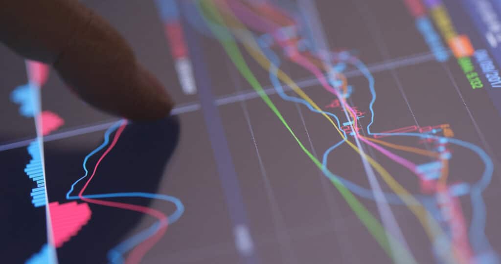 A close-up of a finger pointing at a digital tablet screen displaying colorful, overlapping financial graphs and charts, representing stock market data analysis—ideal for building an Irish brand focused on finance or analytics.