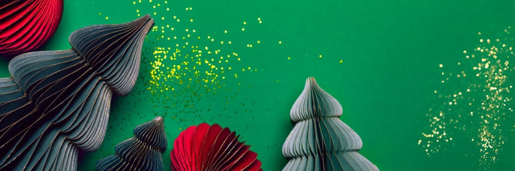 Paper Christmas trees and red ornaments sit on a green background, with gold glitter scattered nearby, creating a festive holiday scene inspired by building an Irish brand.